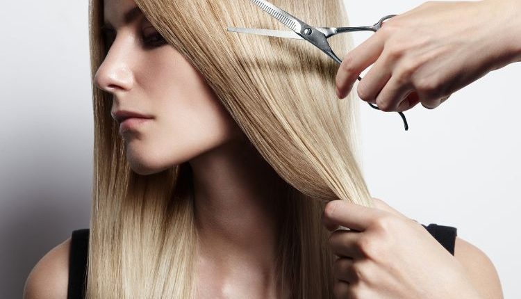 Donna con capelli lunghi e mano con forbici, simbolo di cambiamento e tendenze capelli per la nuova stagione.